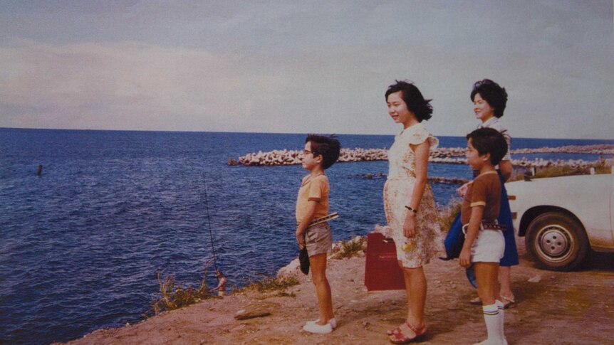 A Japanese woman, two little boys and a teen girl stand on a rocky shore