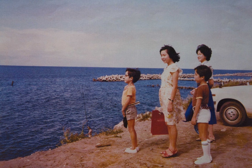 A Japanese woman, two little boys and a teen girl stand on a rocky shore