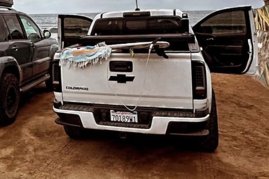 A white ute with a surfboard and towel in the back.