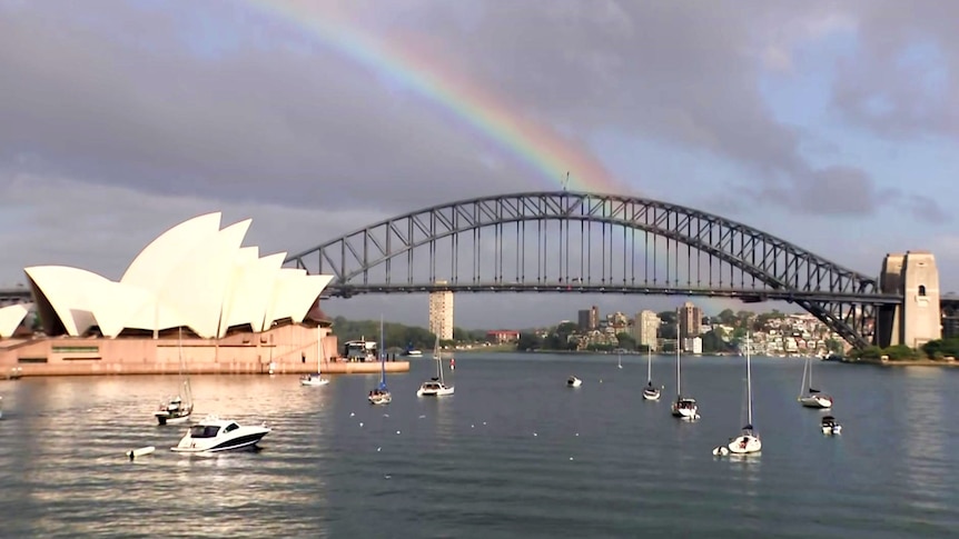 A rainbow over the Sydney Harbour Bridge with boats on the water
