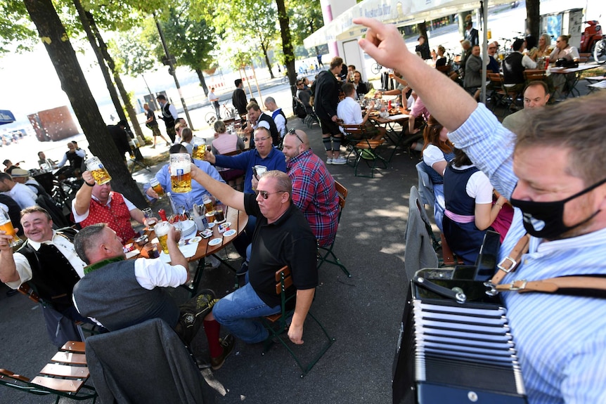 People, some wearing face masks, raise their glasses at a beer garden in Germany.