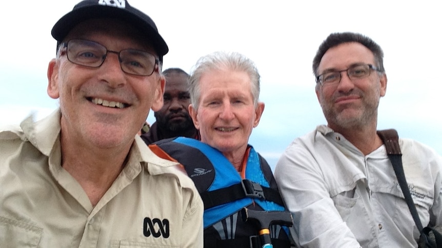 Three men in boat smiling at camera.