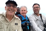 Three men in boat smiling at camera.