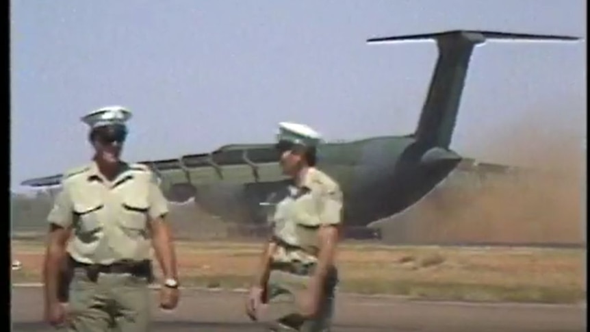 Two people in military unforms stood in front of a military plane. 