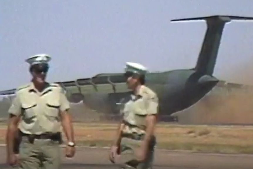 Two people in military unforms stood in front of a military plane. 