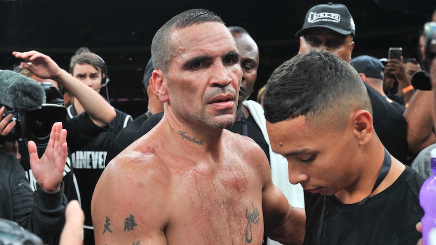 Anthony Mundine, sweating, is surrounded by cameras after a boxing match.