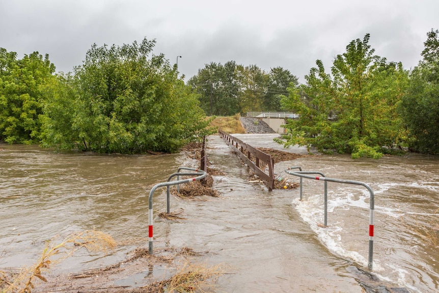 Floodwaters flow over a walkway and foot bridge.