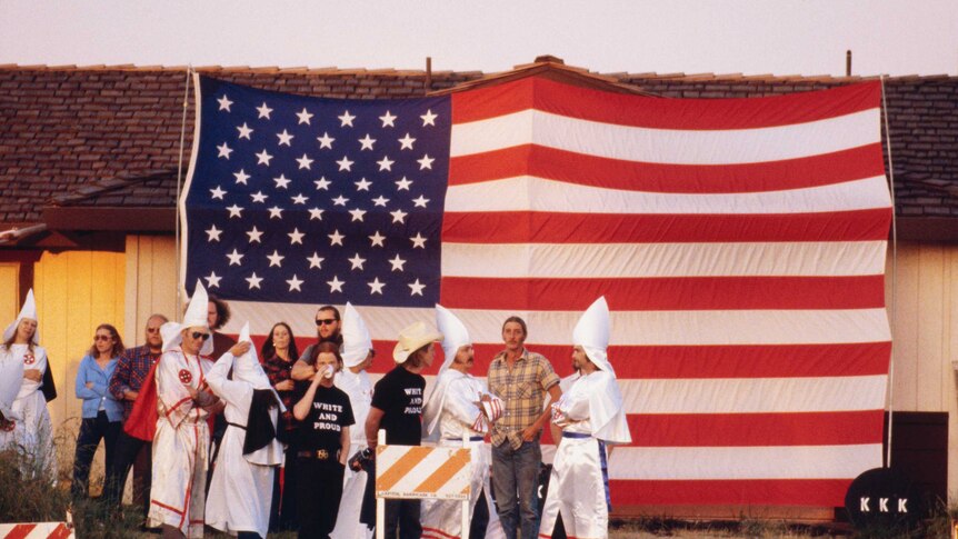 Robed clan members stand in front of an American flag attached to a house during a KKK meeting in Atlanta.