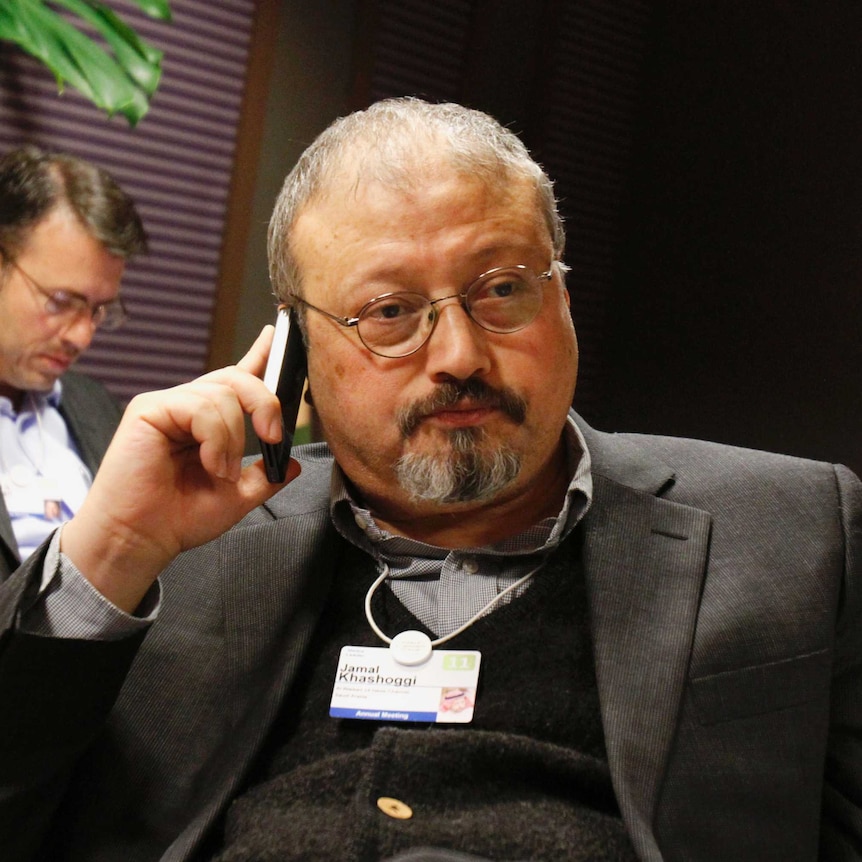 Jamal Khashoggi, wearing a suit and a name, sits in a building talking on a mobile phone with neutral expression