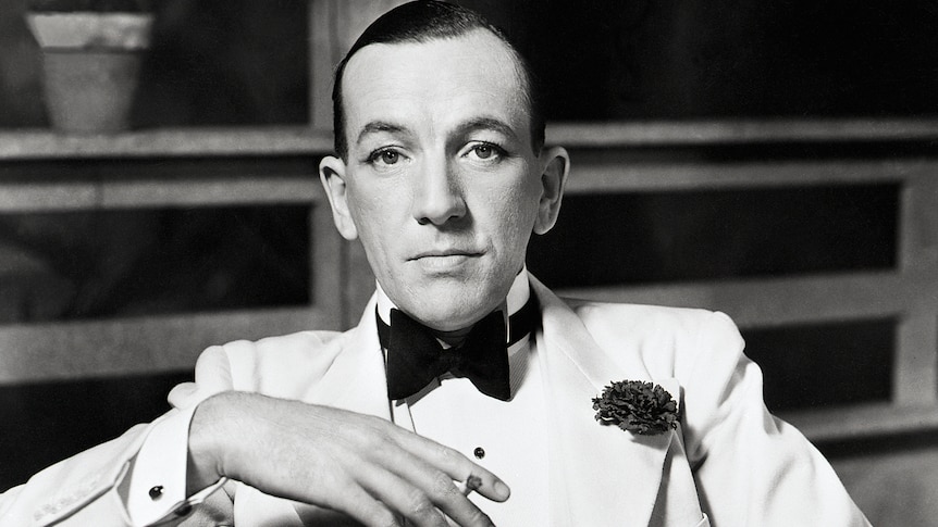 a black and white image of Noel Coward looking into the camera in white tie and very sharp winged eyeliner