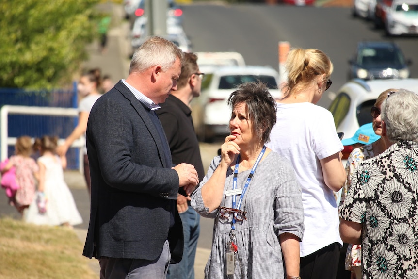 Jeremy Rockliff in a black suit talks to a woman who has her hand to her lip as people stand with facing the other way behind