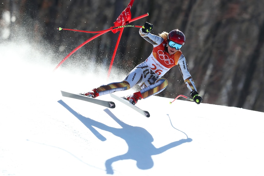 An alpine skiier flies past some marker sticks in the snow