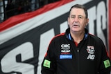 A picture of St Kilda AFL coach Ross Lyon standing on the sidelines at Docklands looking out on the field during a match.