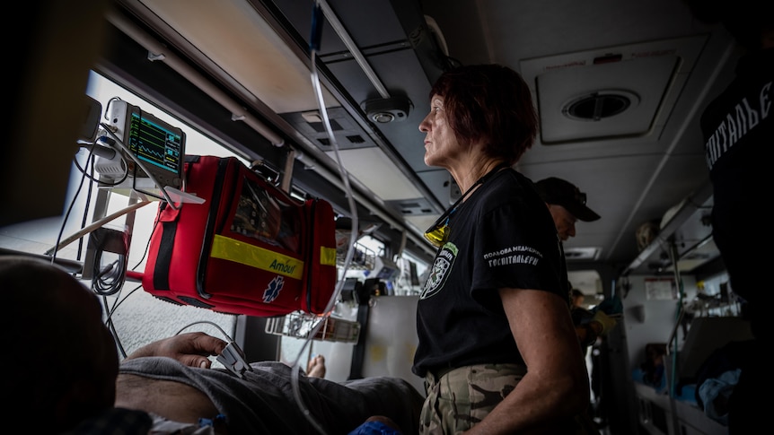 A woman with dark red hair stands on a bus kitted out with hospital beds