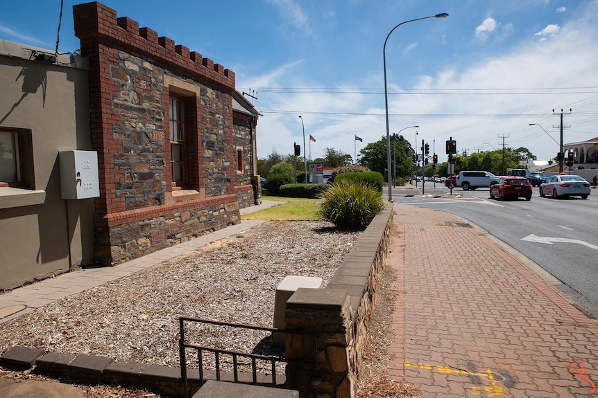 A bluestone wall fronts an intersection where cars wait at a traffic light.