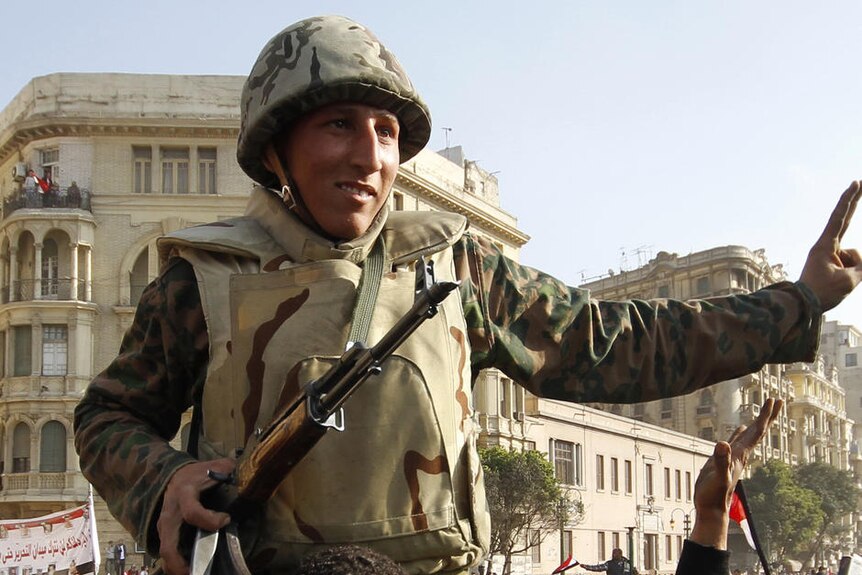 A soldier sits on the shoulders of a protester. A crowd of protesters surround them.