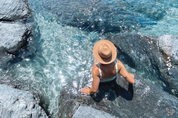 A woman sitting in a rockpool with seawater in it