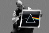 An older gentleman holds up a screen print of Pink Floyd's Dark Side of the Moon artwork