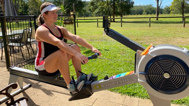 A woman seated on a rowing machine in her backyard