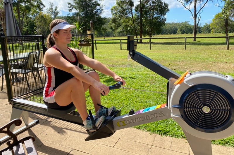 A woman seated on a rowing machine in her backyard