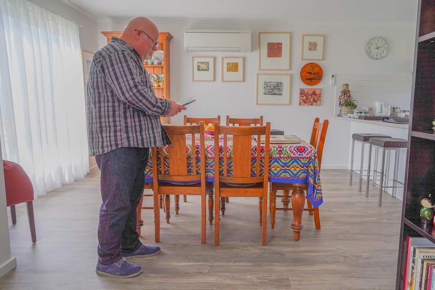 A man stands in a colourfully-decorated kitchen reading a letter.
