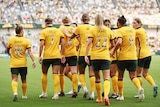 A soccer team wearing yellow and green with rainbow numbers on the back walk away after scoring a goal