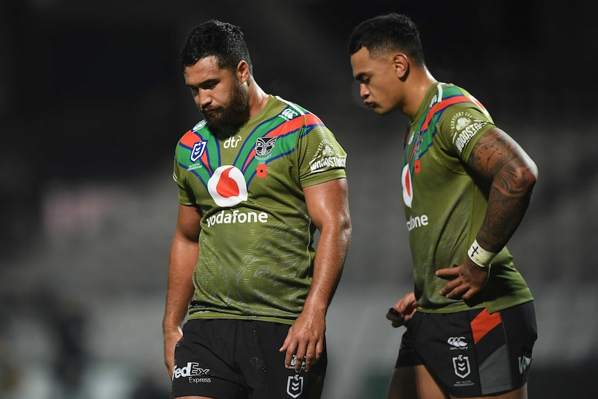 Peta Hiku and Ken Maumalo stand, wearing green shirts, looking down at the ground