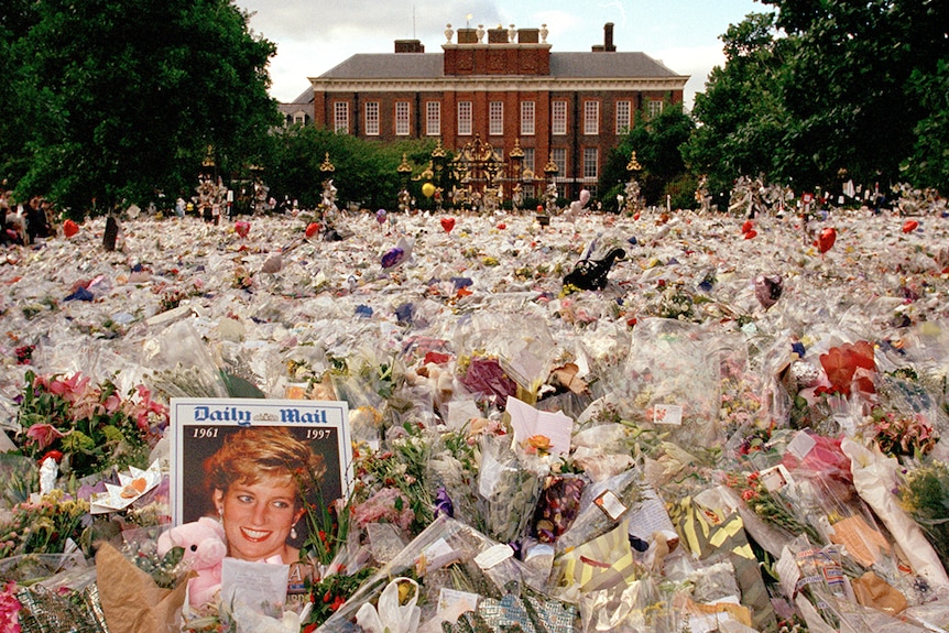 Thousands of flowers laid on the pavement leading to Kensington Palace;  a newspaper featuring Princess Diana in the foreground