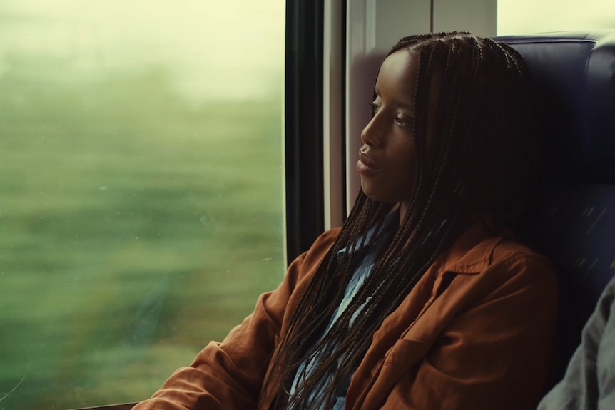 An African American woman sits alone on a train, staring out the window.