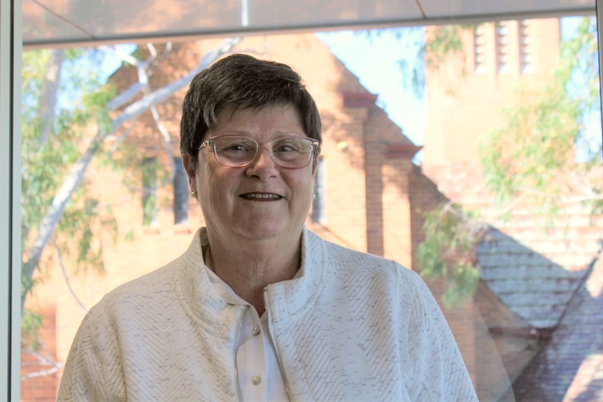 A woman in a white shirt smiles at the camera.