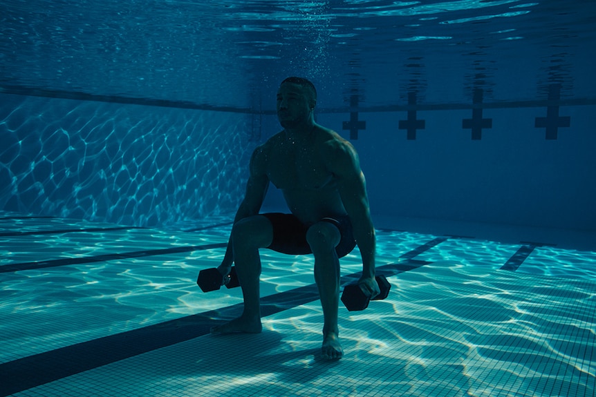 Colour still of Michael B Jordan lifting weights underwater in 2018 film Creed II.