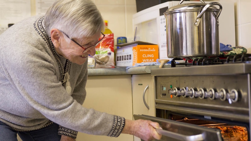 Elderly woman Lesley Drake opens oven in kitchen.