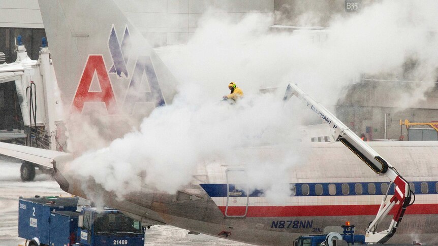 An American Airlines crew member sprays de-icing solution on a plane during a snowstorm in Boston, Massachusetts.