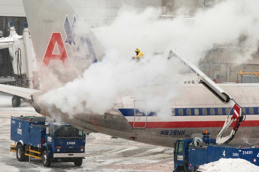 An American Airlines crew member sprays de-icing solution on a plane during a snowstorm in Boston, Massachusetts.