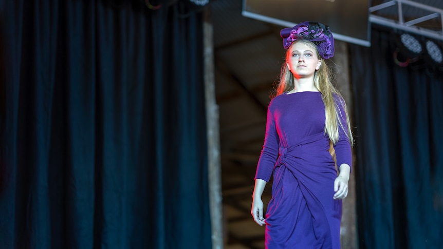 A woman in a purple dress walks on a runway.