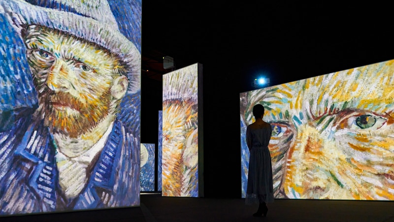 darkened gallery space with digital projections of Van Gogh's self-portraits.