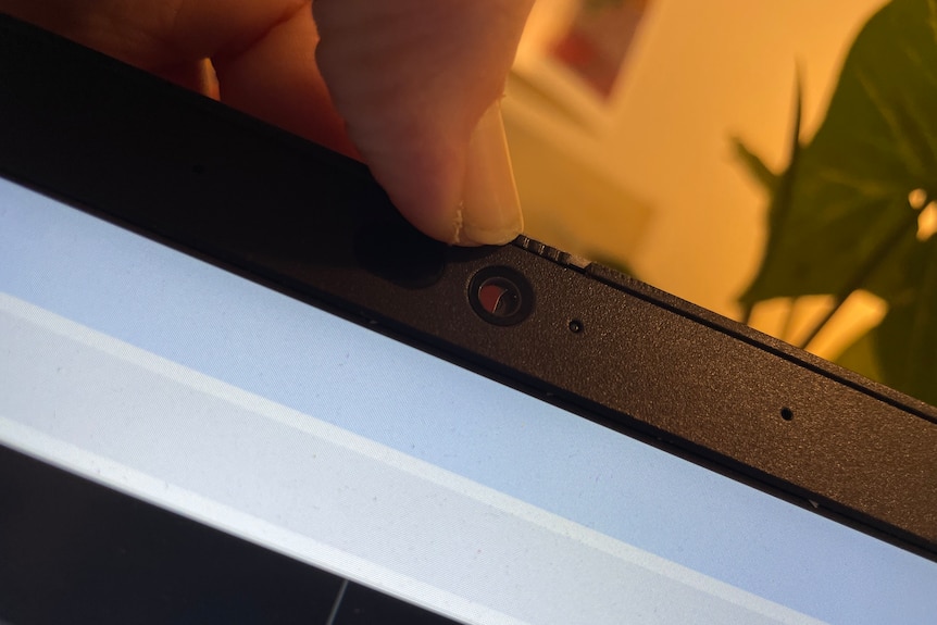 A person's thumb sliding the webcam cover over a laptop's camera lens. 