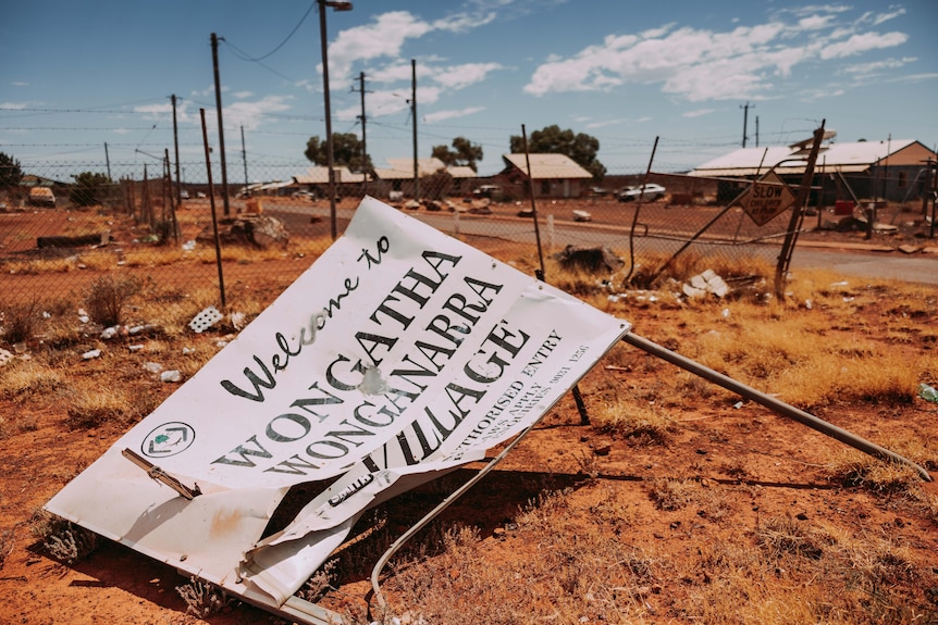 A broken sign lying on the ground at a desert settlement.