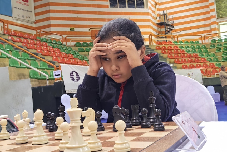 Young girl holds hands to forehead while looking at a chessboard. 