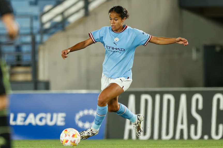 A woman football player wearing light blue and white goes to kick the ball during a game