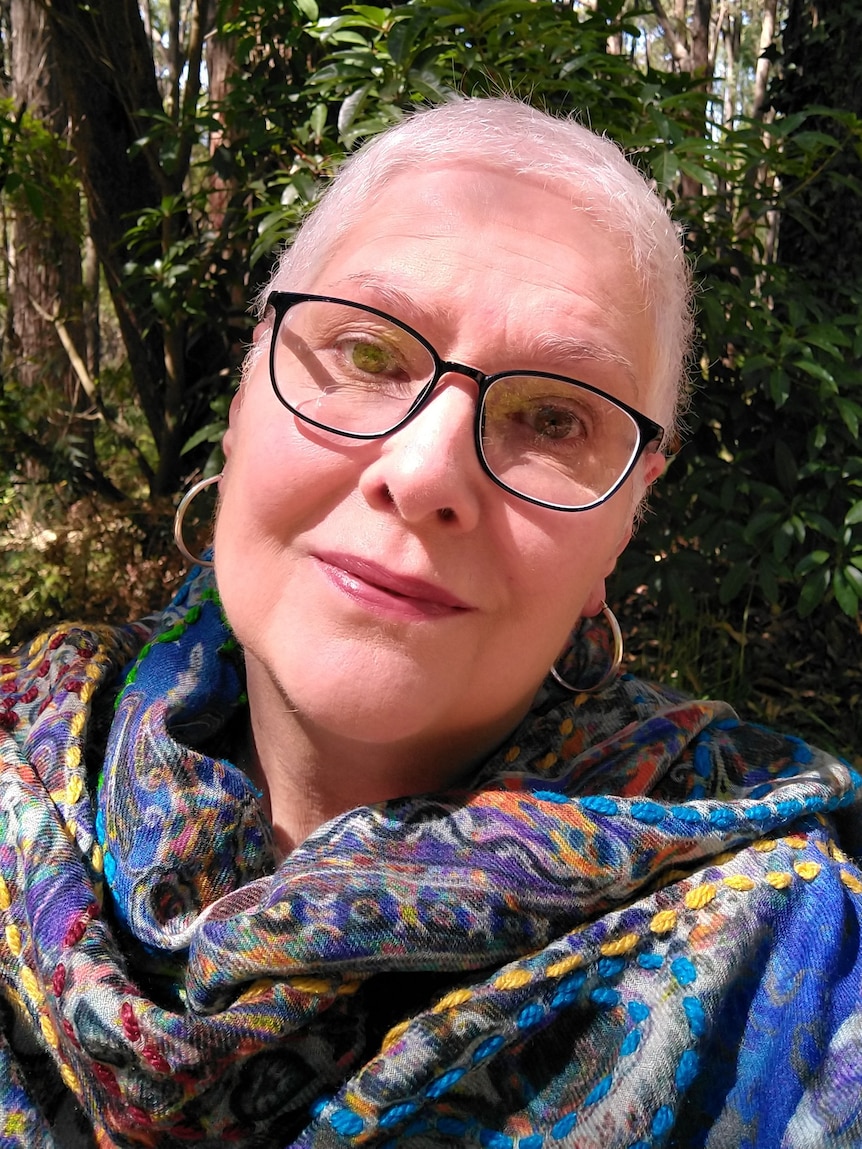 A portrait of a woman with hoop earrings, glasses and a brightly coloured scarf.