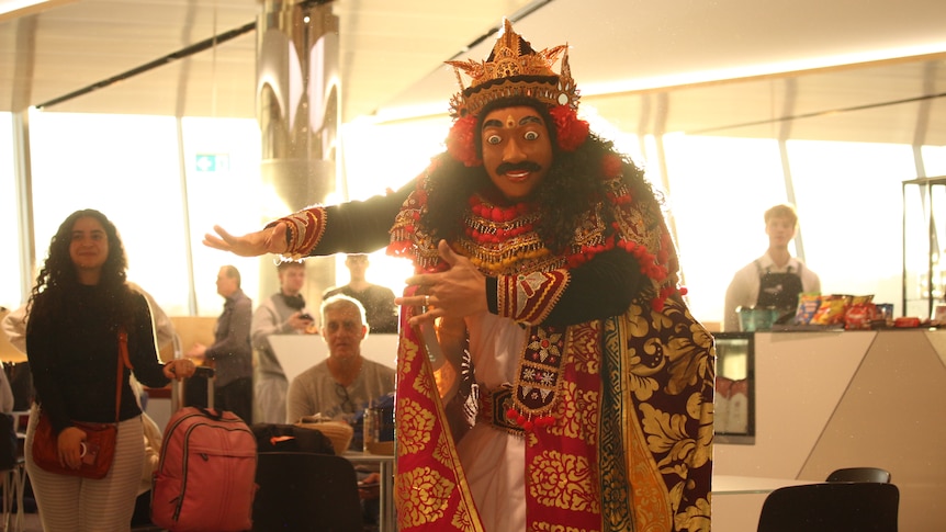 A person wearing cultural clothing including colorful robes, headwear and a mask performs a dance.