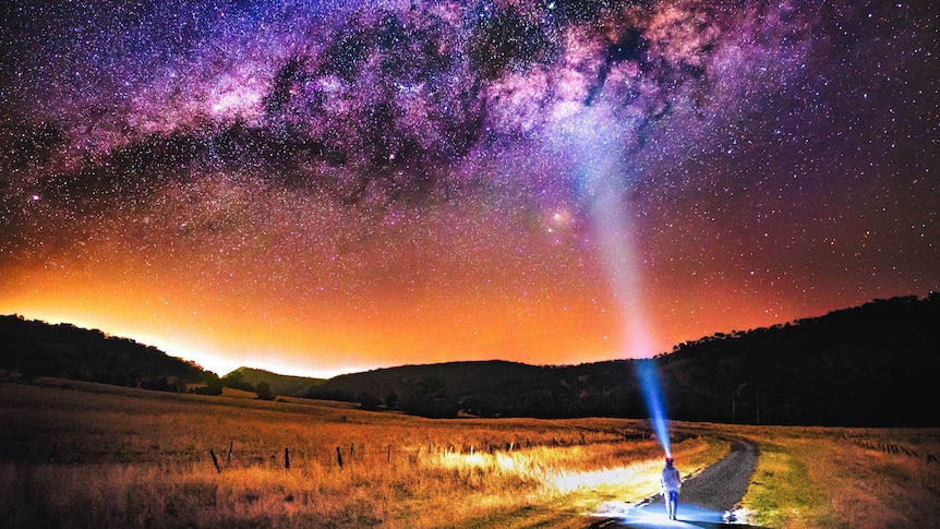 A man looks up at the Milky Way from a country road at night.