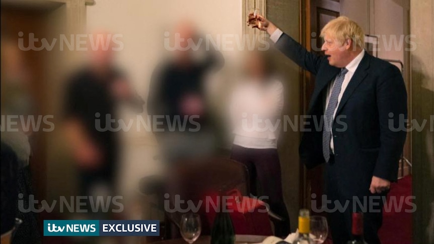 ITV-watermarked image shows four people intentionally blurred as a man in a suit with a white flop of hair raises his glass