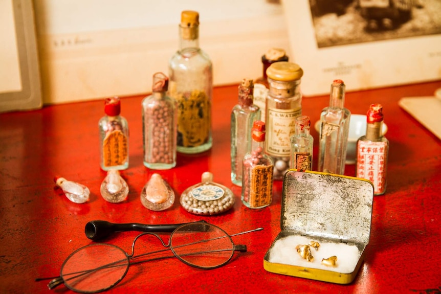 Close-up view of objects including glasses, small Chinese medicine bottles and gold false teeth in a tin.