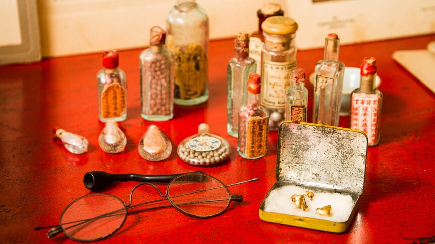Close-up view of objects including glasses, small Chinese medicine bottles and gold false teeth in a tin.