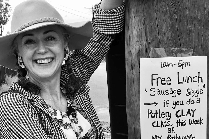 Woman in akubra hat smiles next to sign that says 'Free sausage sizzle if you do a pottery class this week'.