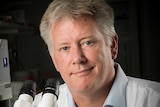 A man smiles to camera in front of a microscope.