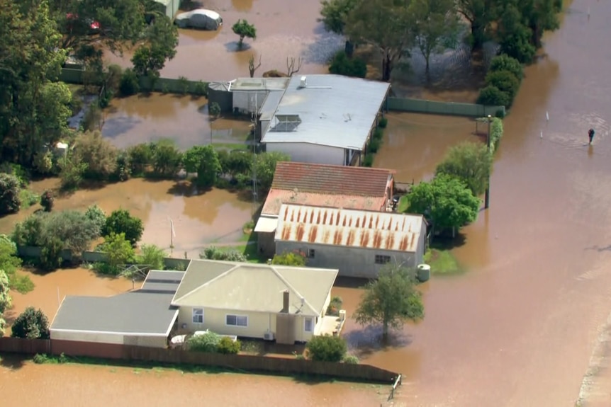 An aerial shot of brown murky flood waters surrounding several properties and a person walking through the water