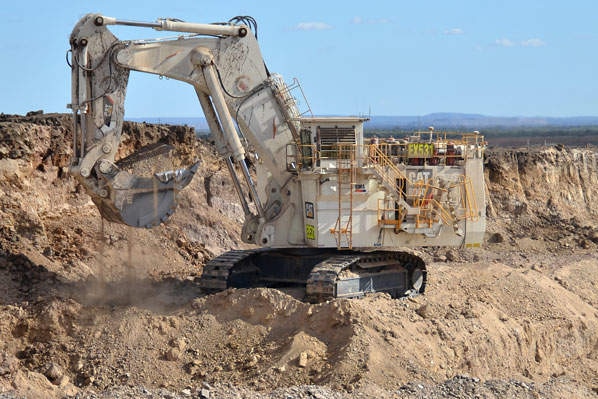 A large excavator at work on a dusty mining site.